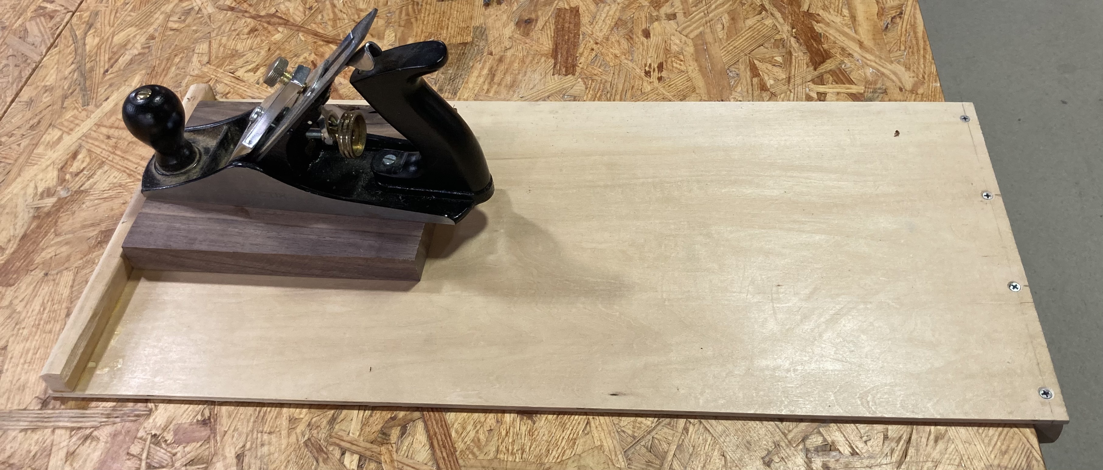 Stock that rests against the hook at the end of a plane board. This is one of several jigs that can be used to support a board for hand planing. Instead of fully clamping the board, it provides a stop that resists movement in the single direction that the planing operation applies force.